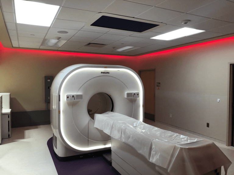A modern medical imaging room featuring a K2 Electric Philips CT scanner, encased in a sleek white cover and illuminated by ceiling lights with a red accent.