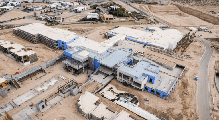 Aerial view of a large construction site with several partially constructed buildings, surrounded by cleared land and existing infrastructure from K2 Electric.