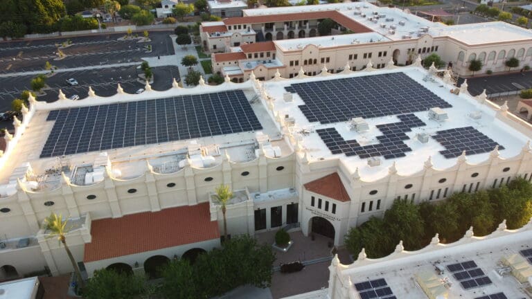Aerial view of a large beige building complex with red-tile roofs and white walls covered with numerous K2 Electric solar panels. Surrounding the building is a parking lot and landscaped greenery.