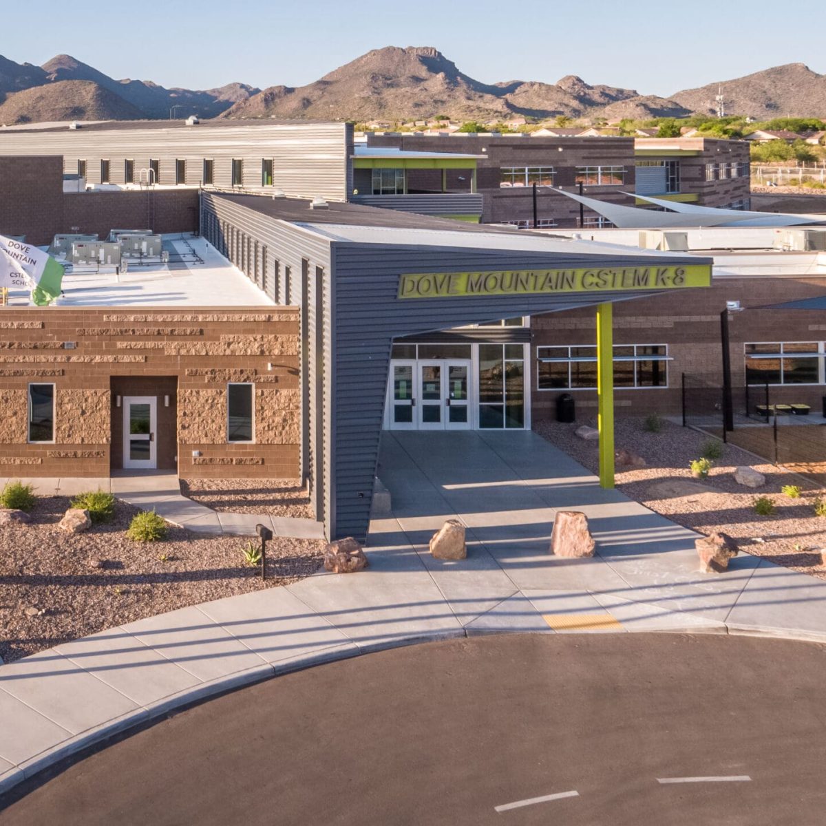 Exterior view of a large construction desert school building with multiple flags, including the U.S. and Arizona flags, featuring a modern design and mountainous backdrop.